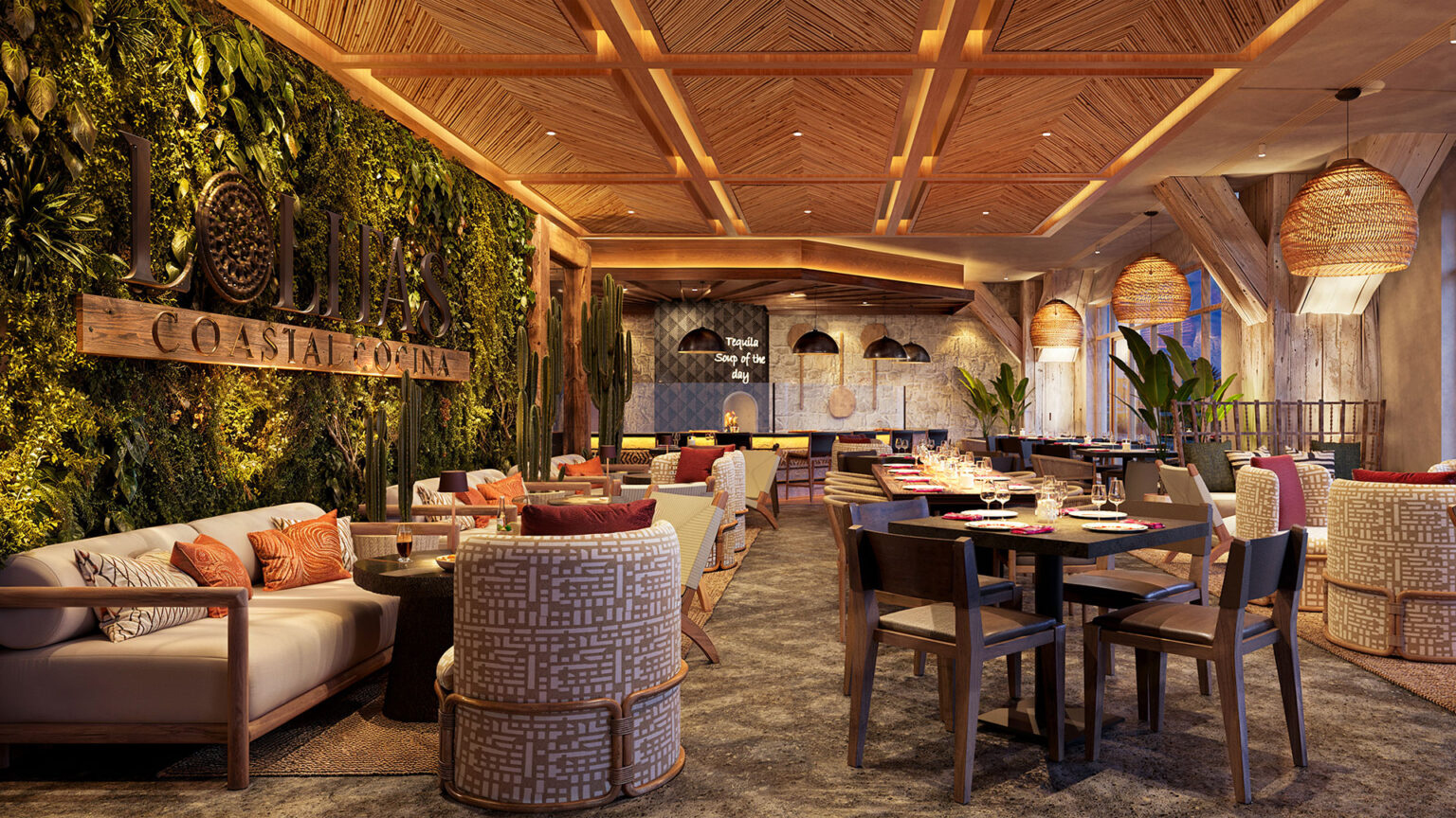 A cozy, upscale restaurant interior with wooden ceilings and a green plant wall evokes the charm of new hotels in Clearwater Beach, Florida. Tables are set for dining, surrounded by cushioned chairs. Warm hanging lights add to the inviting atmosphere, with signage reading Lobita Coastal Cantina.