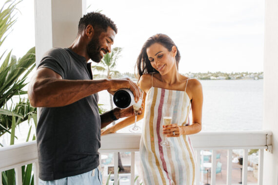 A couple drinking champagne on a private balcony with the ocean in the background at Opal Key Resort & Marina.